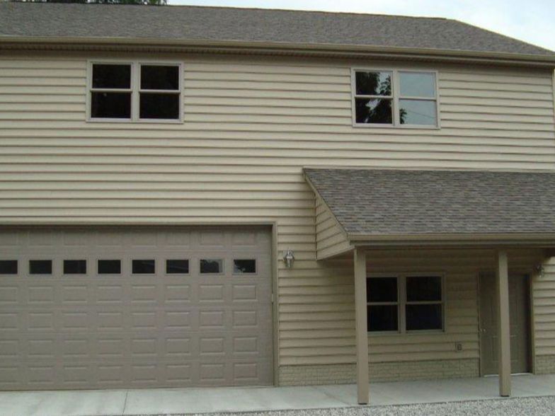 Beige two-story house with a garage and small porch. Two windows on the upper level.