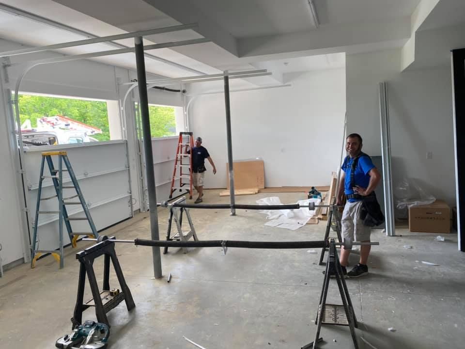 Two men installing a garage door in a mostly empty room, using tools and a ladder.