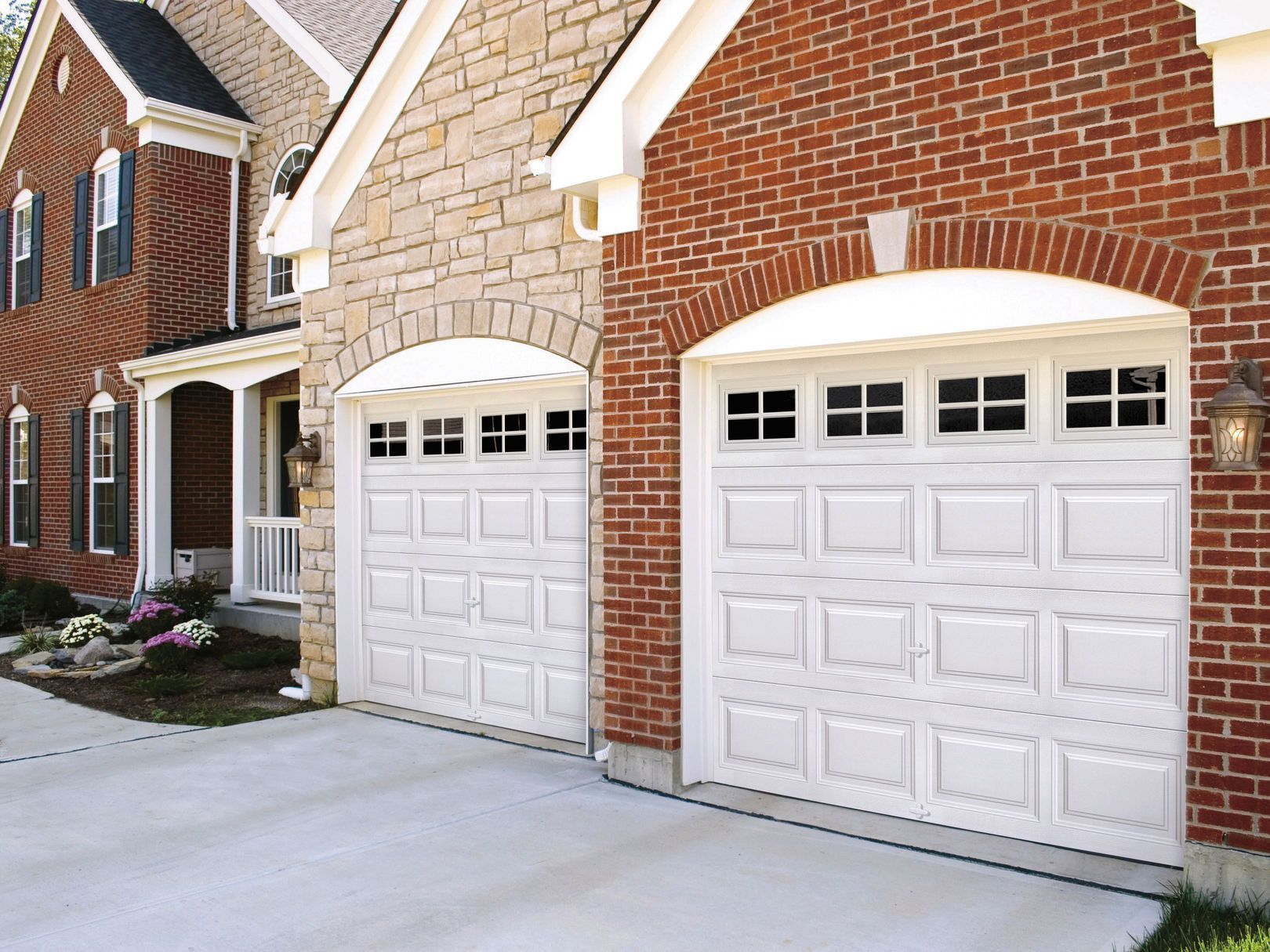 Two white garage doors, arched, on houses of brick and stone.