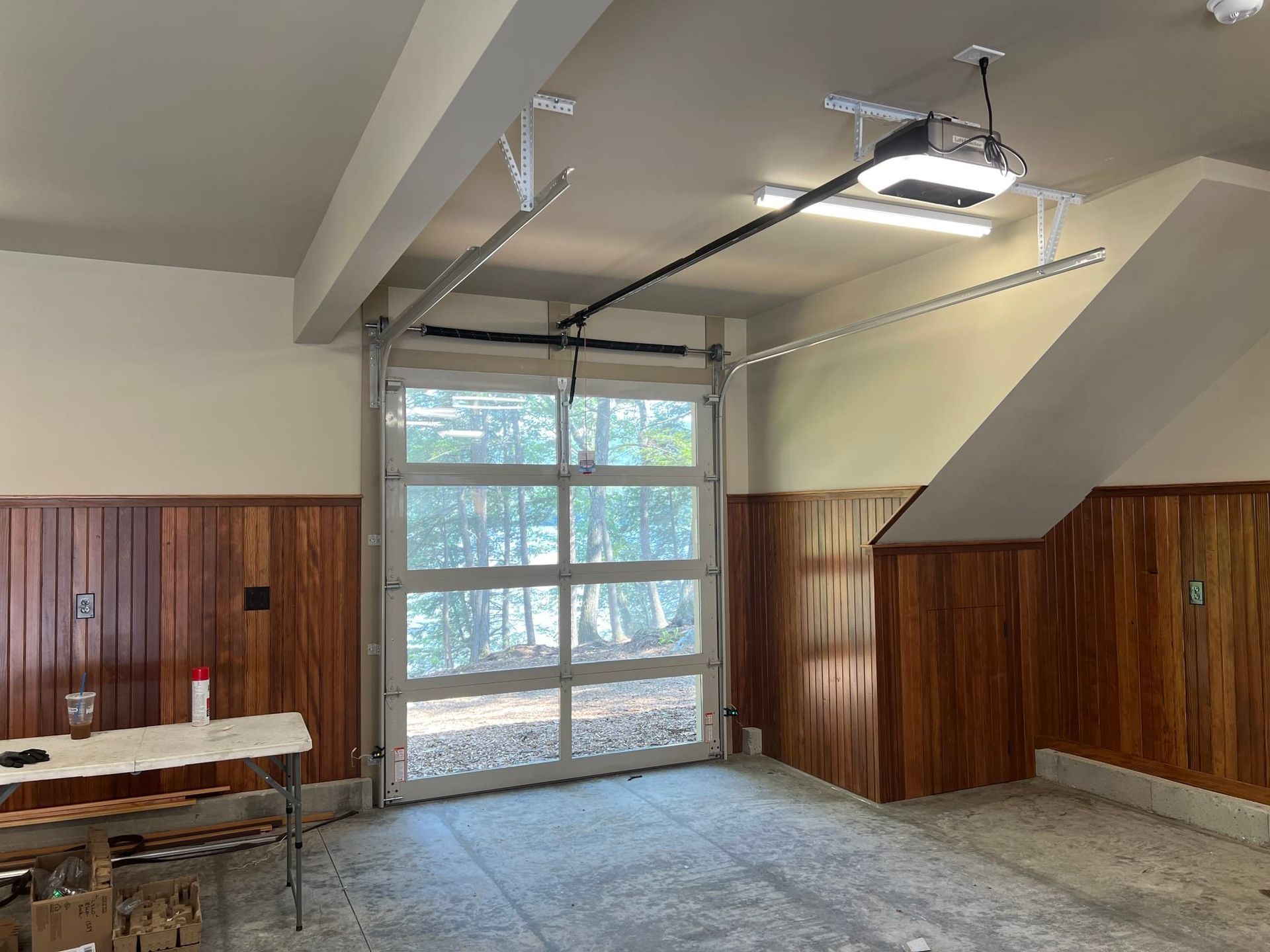 Garage interior with glass garage door, wood paneling, and concrete floor.