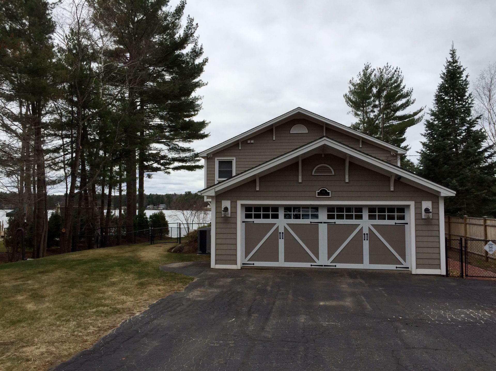 Two-story tan garage with white accents, trees, and driveway. Overcast sky.