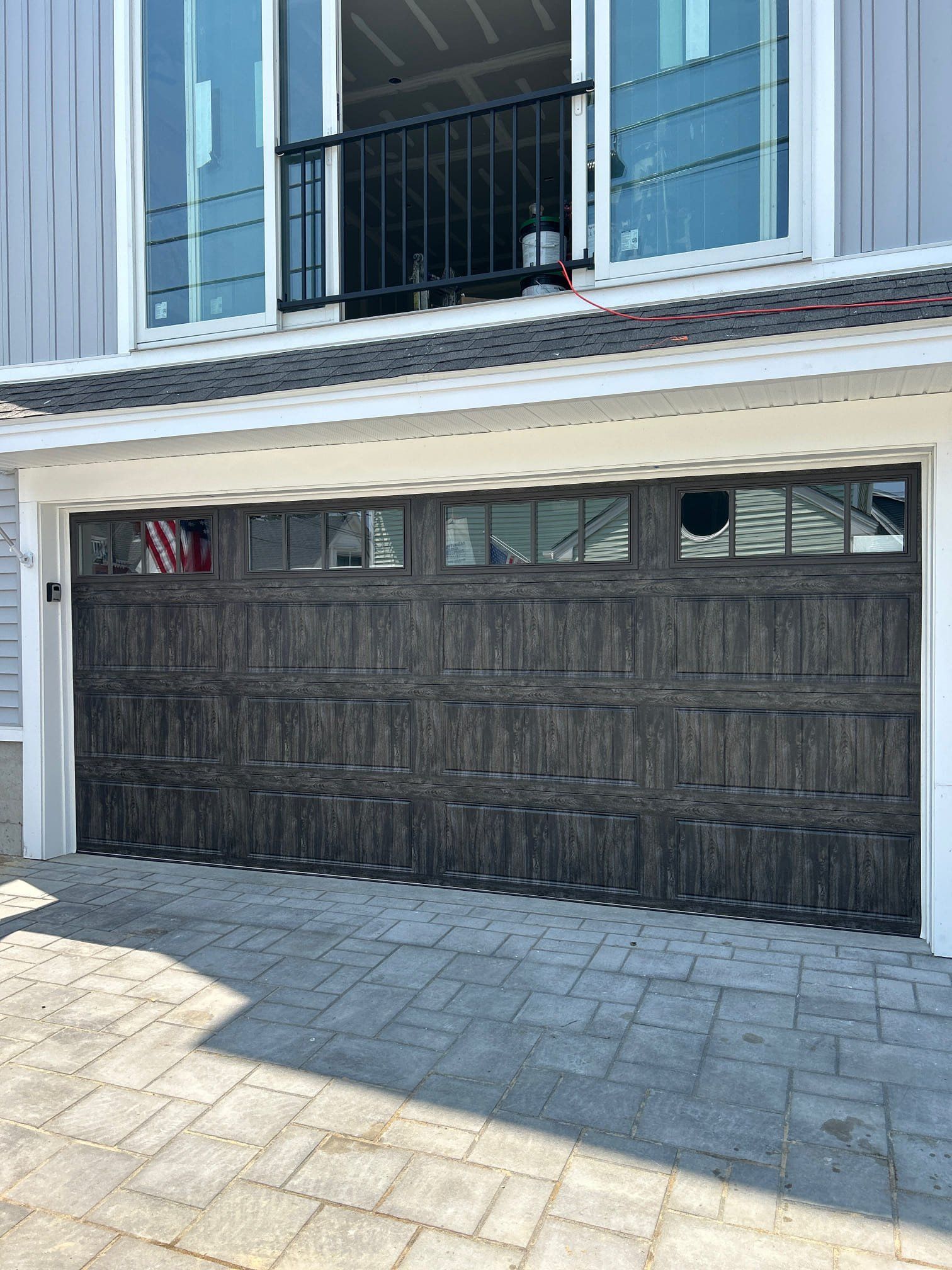 Dark gray garage door with windows below a balcony and large windows.