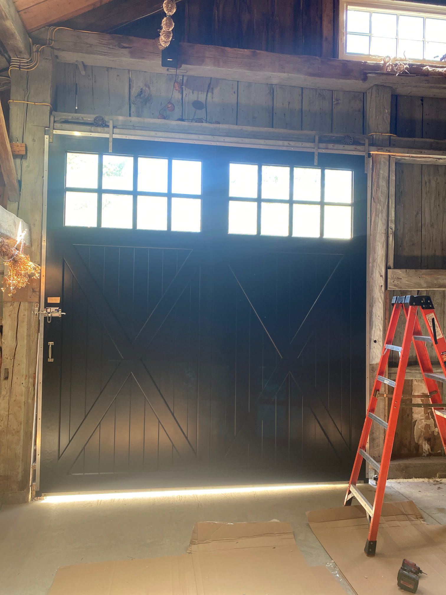 Black barn door with glass panes, ladder to the right, inside a barn.