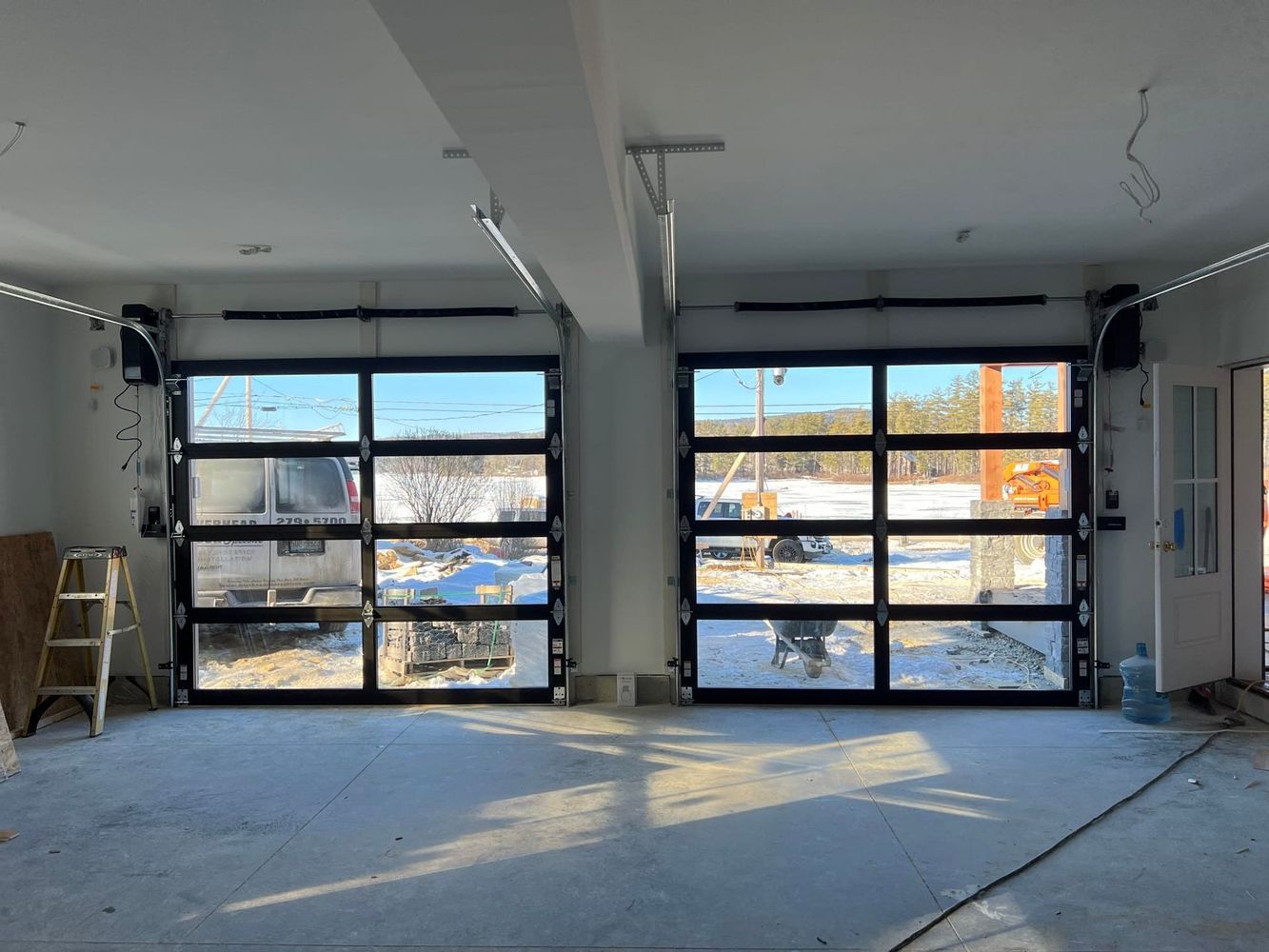 Two glass garage doors with black frames in a light-filled interior. Snow visible outside.