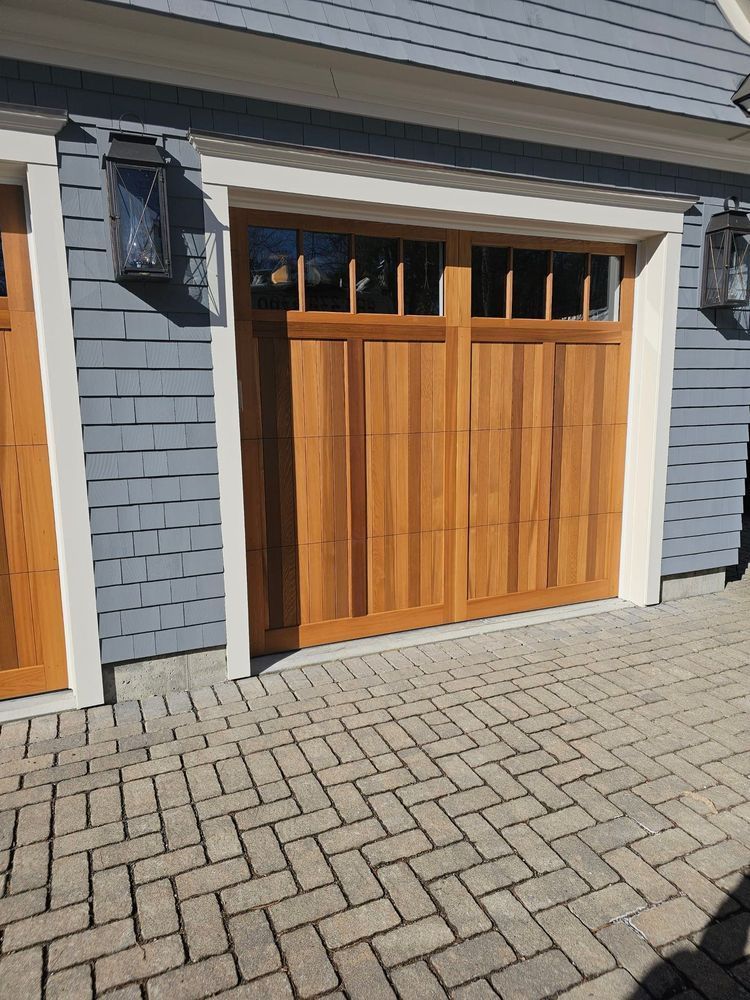 Wooden garage door with windows, surrounded by blue siding and a brick walkway.