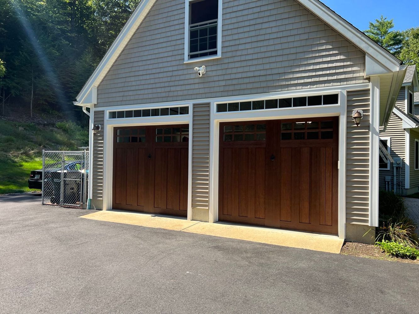 Two-car garage with brown doors, tan trim, and light gray siding on a sunny day.