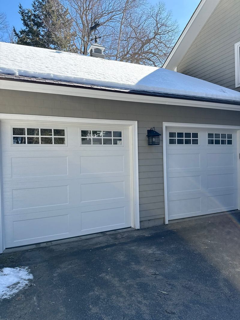 White garage doors with windows, snow on roof, light gray siding.