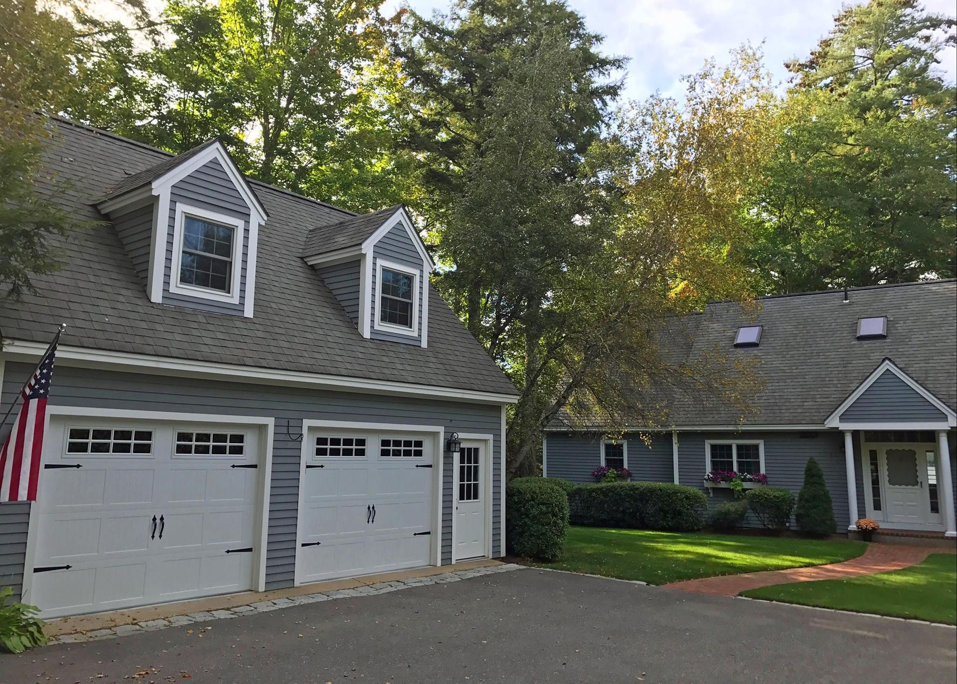 Two-story blue house with white garage doors and American flag; green trees in background.