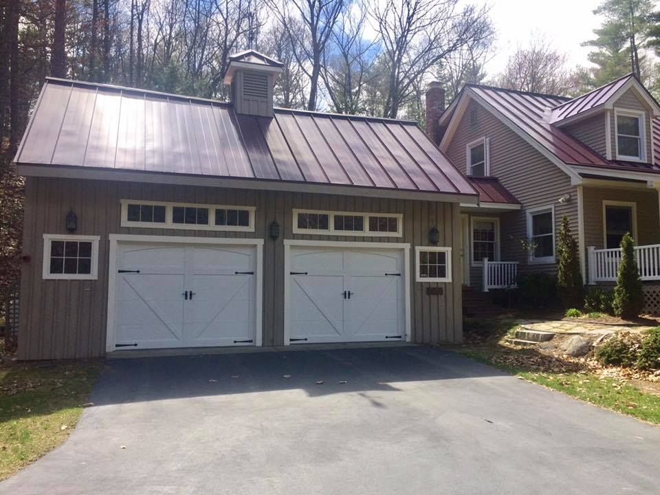 Two-car garage with white doors, attached to a house with red roof, surrounded by greenery.
