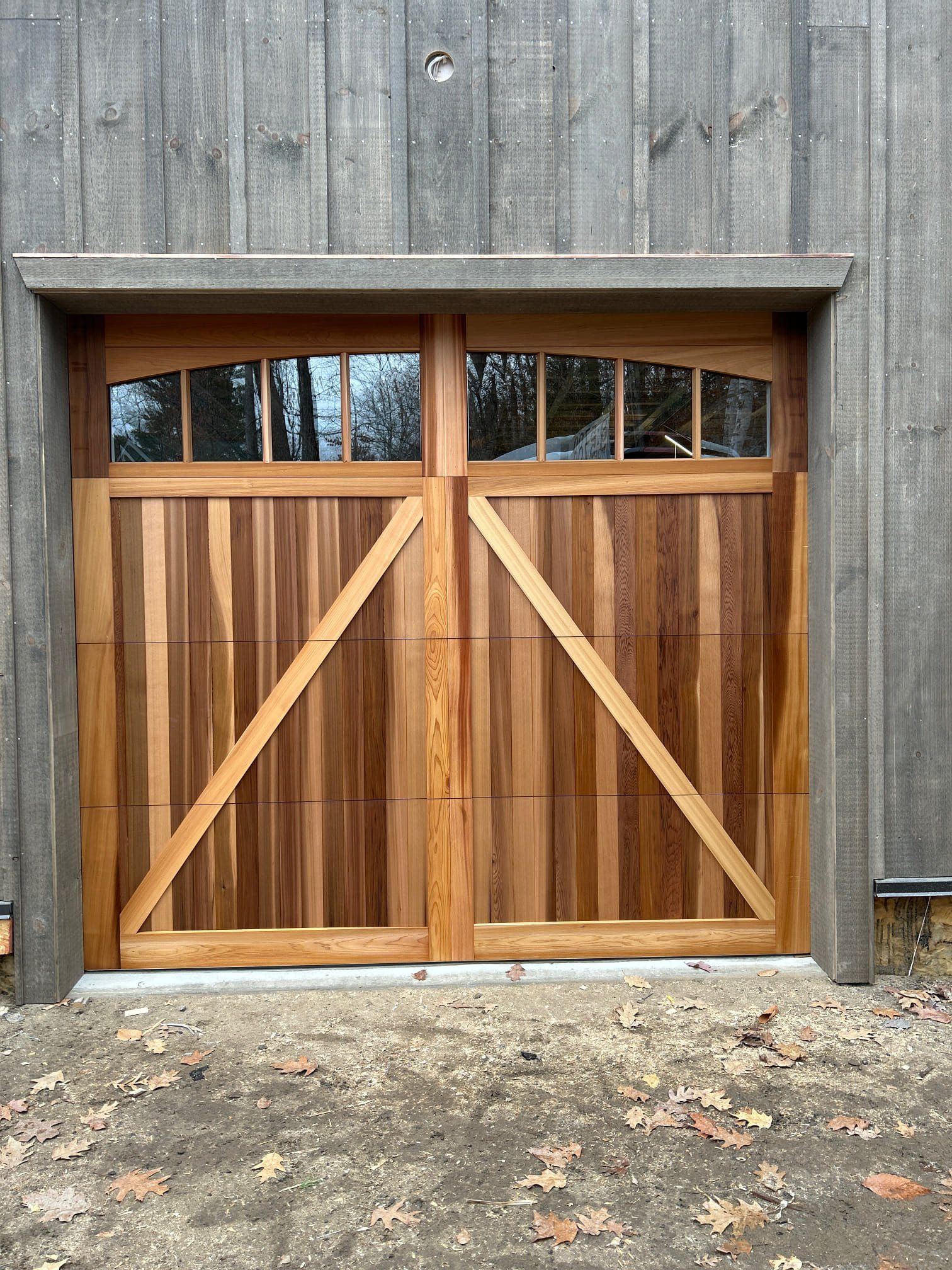 Wooden garage doors with arched windows and diagonal supports.