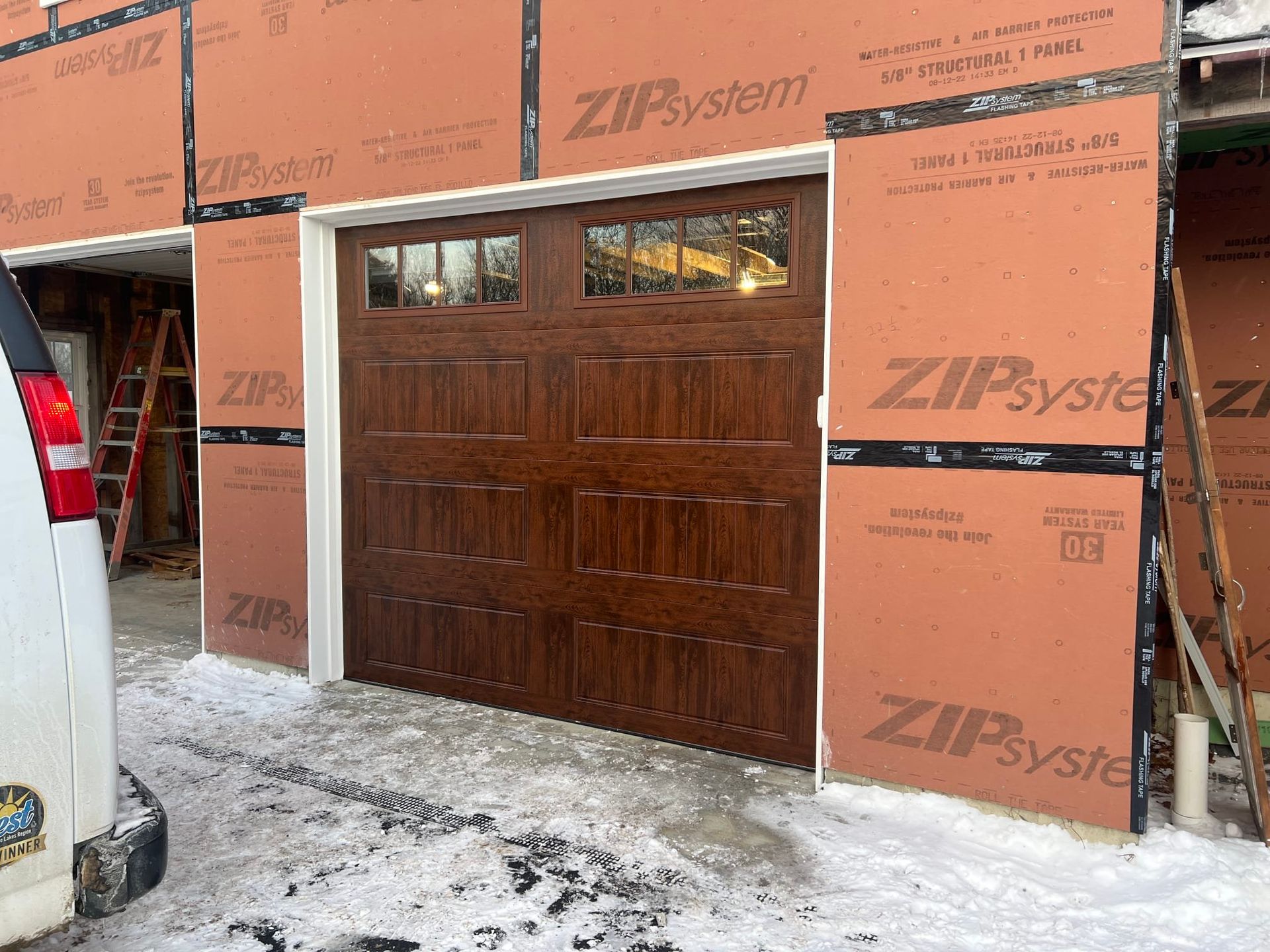 Brown garage door in a new construction setting, surrounded by orange sheathing and white trim.