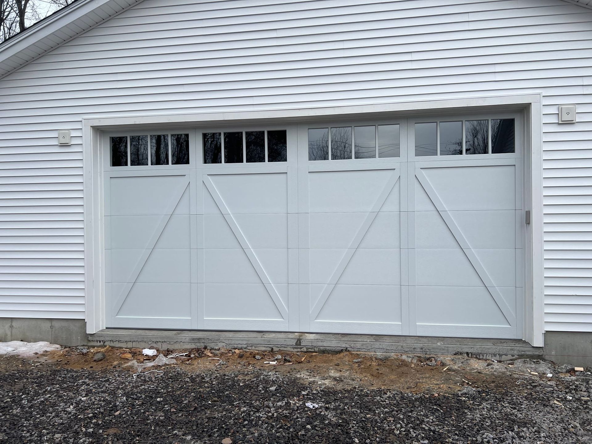 White garage door with windows, on a white building with visible snow on the ground.