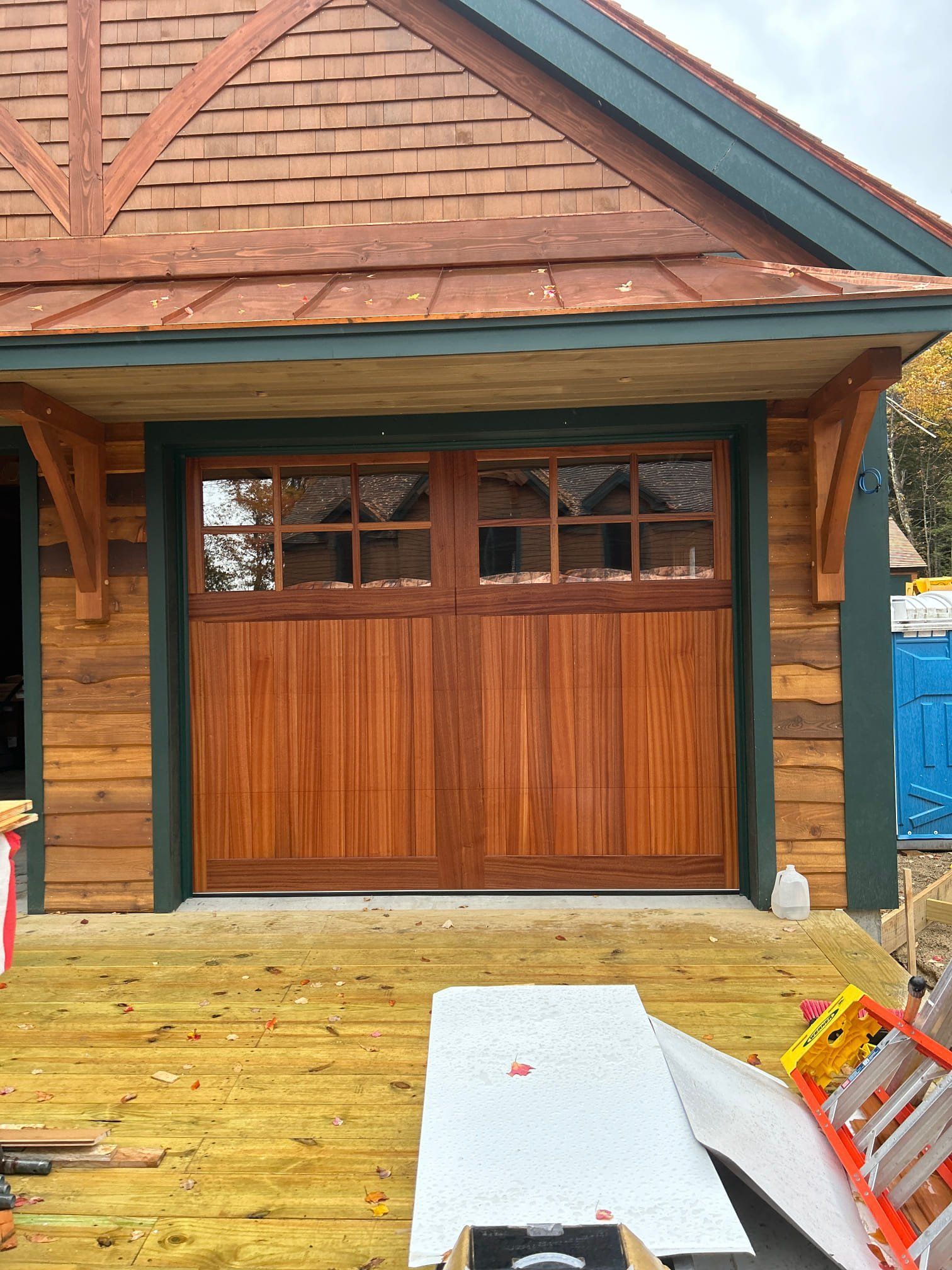 Wooden garage door with windowed top panels, set in a wood-paneled building with a brown roof.