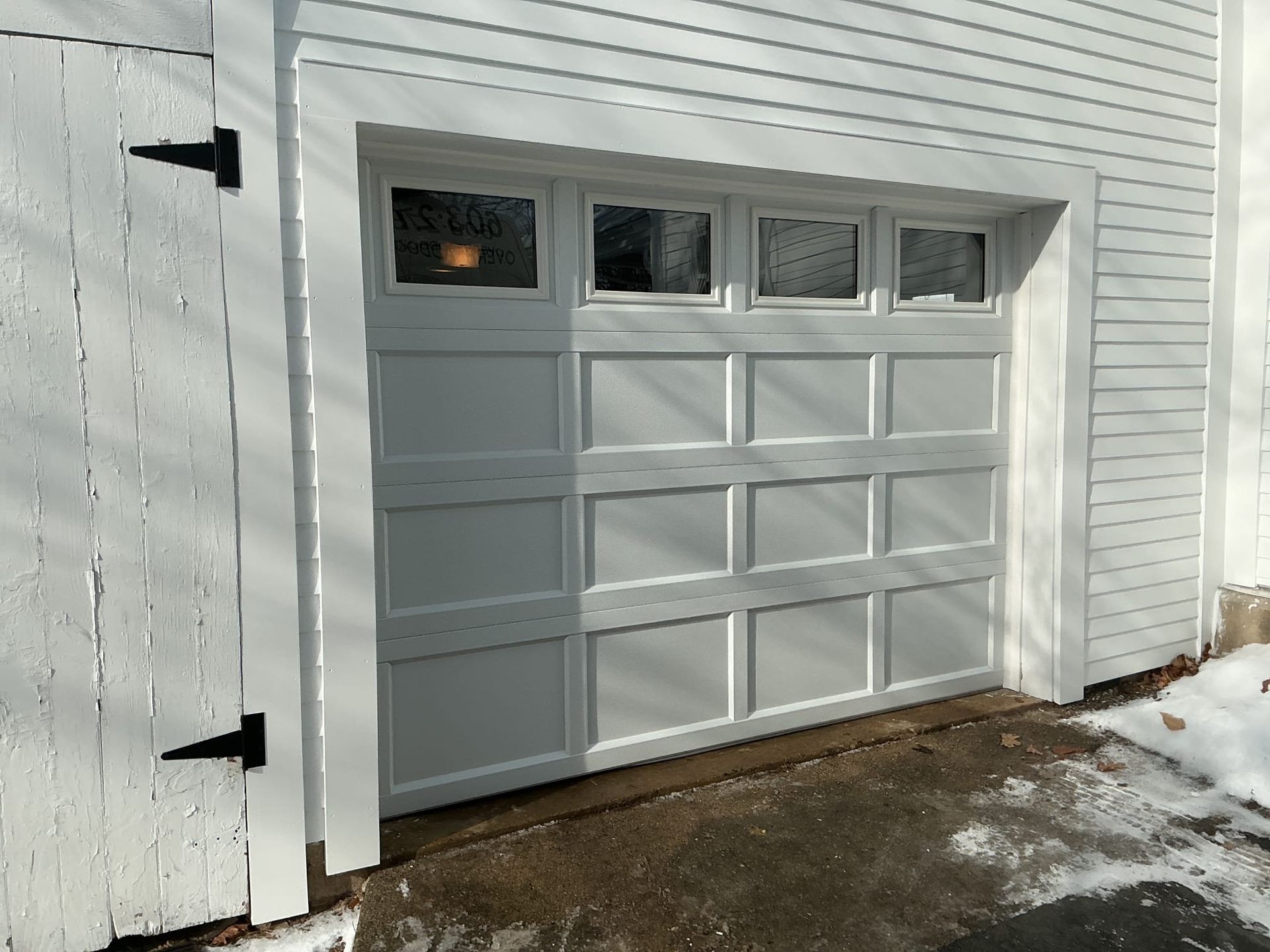 White garage door with window panels and a wooden side door with black hinges.