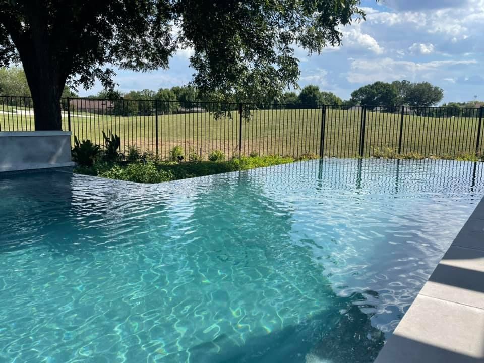 A large swimming pool with a fence around it and a tree in the background.
