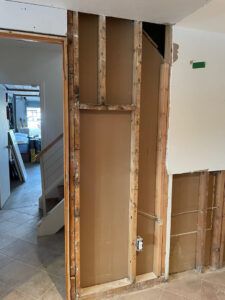 Exposed wooden wall studs and drywall backing in a home renovation area next to an open doorway leading to a staircase.