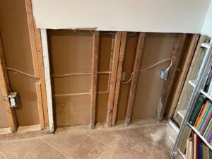 An open wall revealing wooden studs, electrical wiring, and electrical outlet boxes in an unfinished room.