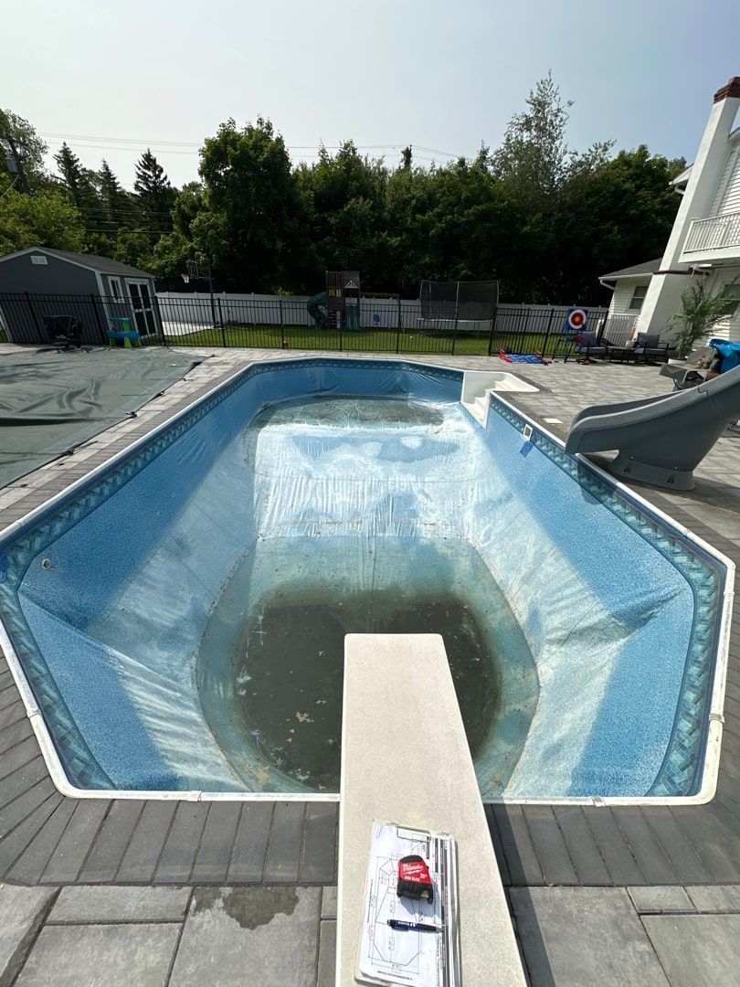 An empty, blue-patterned inground swimming pool with a diving board in the foreground and a slide on the right.