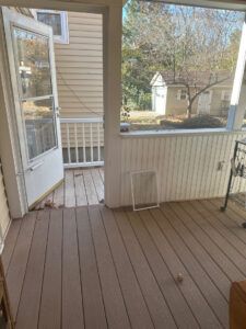 A view from inside a covered porch looking out through a door toward a neighboring house with a yard.