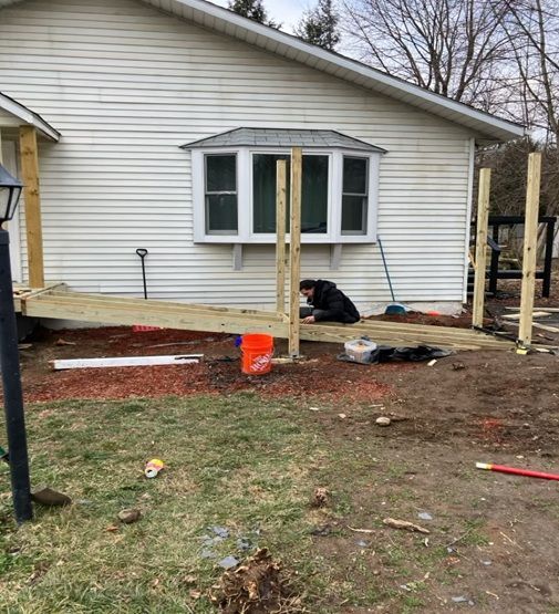 A person works on the wooden frame of an outdoor residential wheelchair ramp attached to a house.