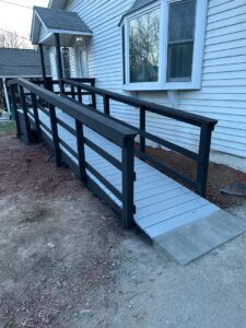 A wooden wheelchair ramp with black railings leading to the side entrance of a white house.