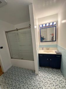 Bathroom with a navy vanity, square mirror with lights, and a glass-enclosed shower on a blue mosaic tiled floor.