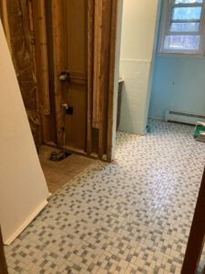 A bathroom under renovation with exposed wooden wall studs, plumbing fixtures, and tiled flooring.
