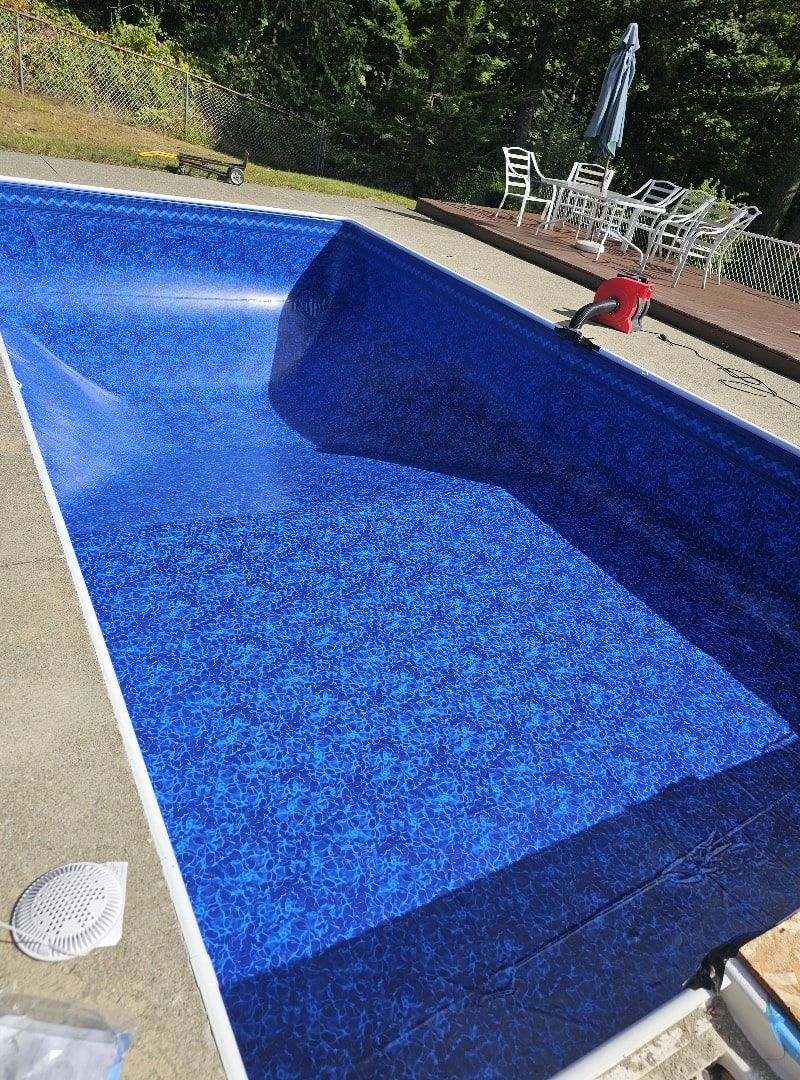 An empty, deep blue patterned swimming pool with a sloped floor, next to a patio with outdoor furniture.
