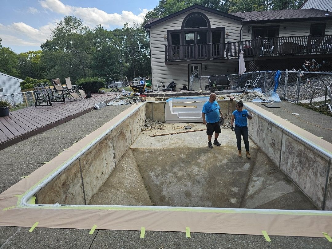 Two people standing inside a drained, empty backyard swimming pool undergoing renovation near a house.