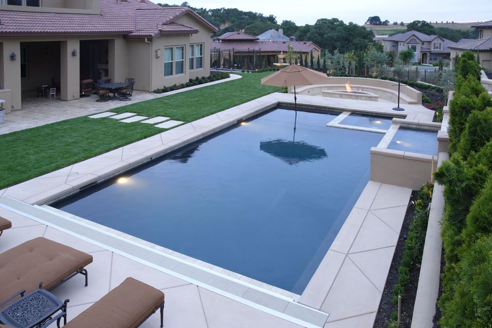 A rectangular swimming pool with a spa, adjacent lawn, and patio furniture in a suburban backyard.