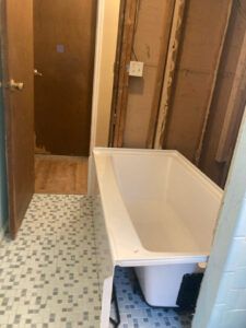 A white bathtub placed in a bathroom undergoing renovation with exposed wall studs and partially tiled floors.