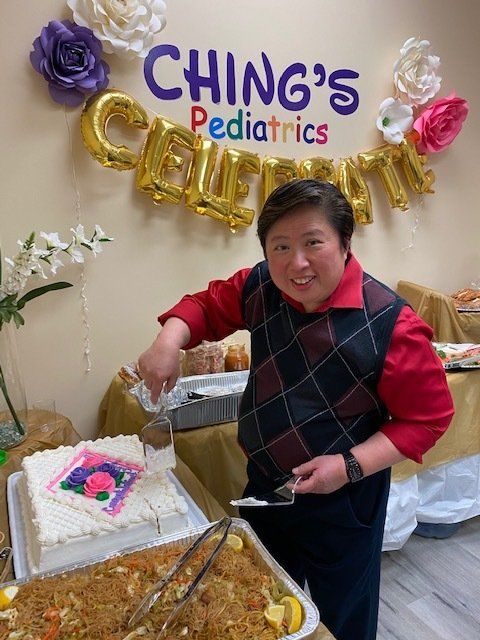 A man is cutting a cake in front of a sign that says ching 's pediatrics