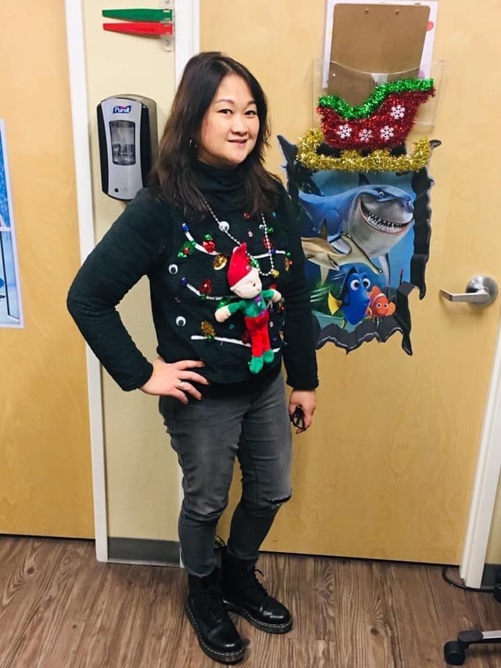 A woman wearing a christmas sweater is standing in front of a door.