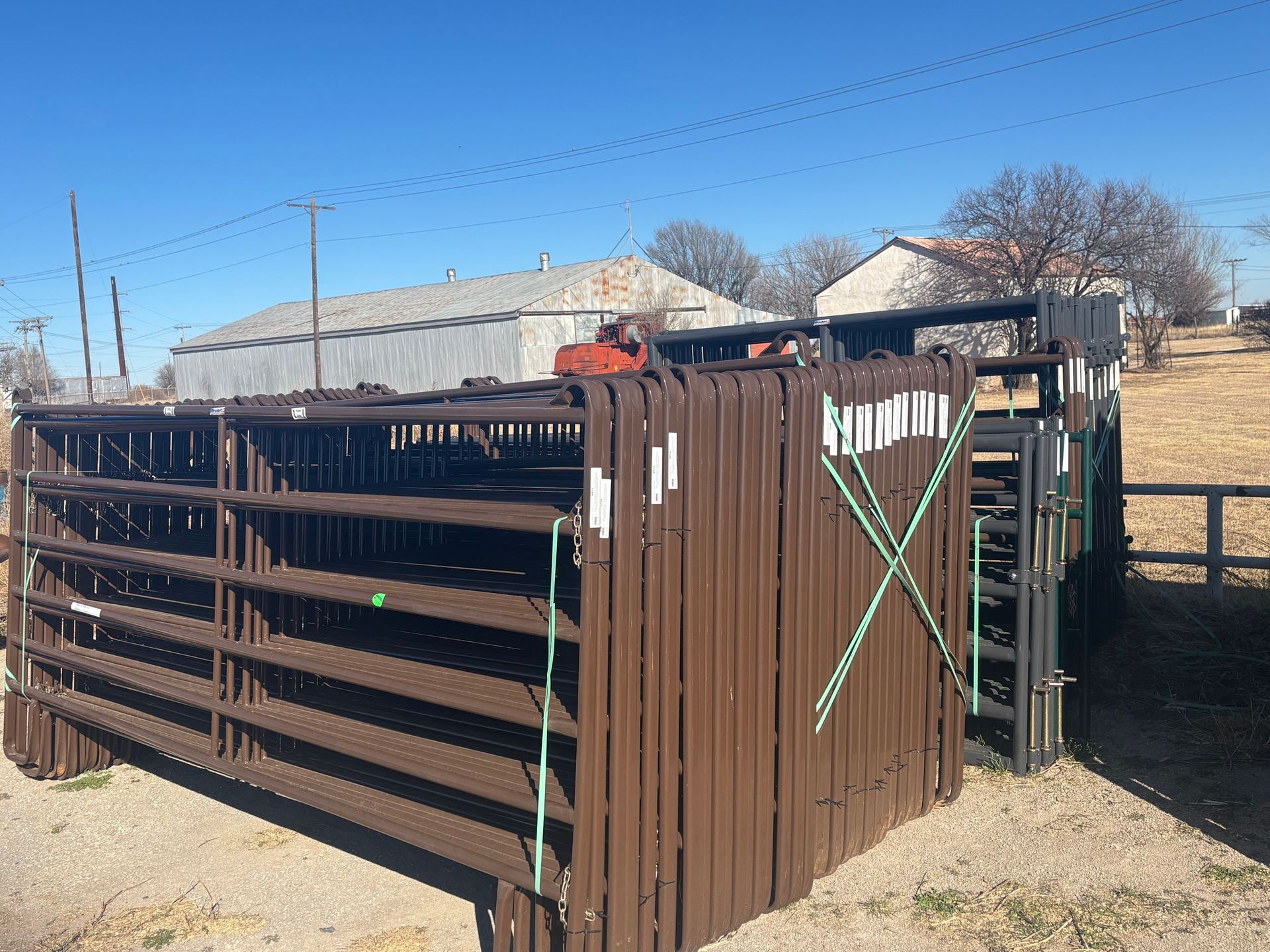 A stack of brown metal livestock panels secured with straps outdoors on a sunny day.
