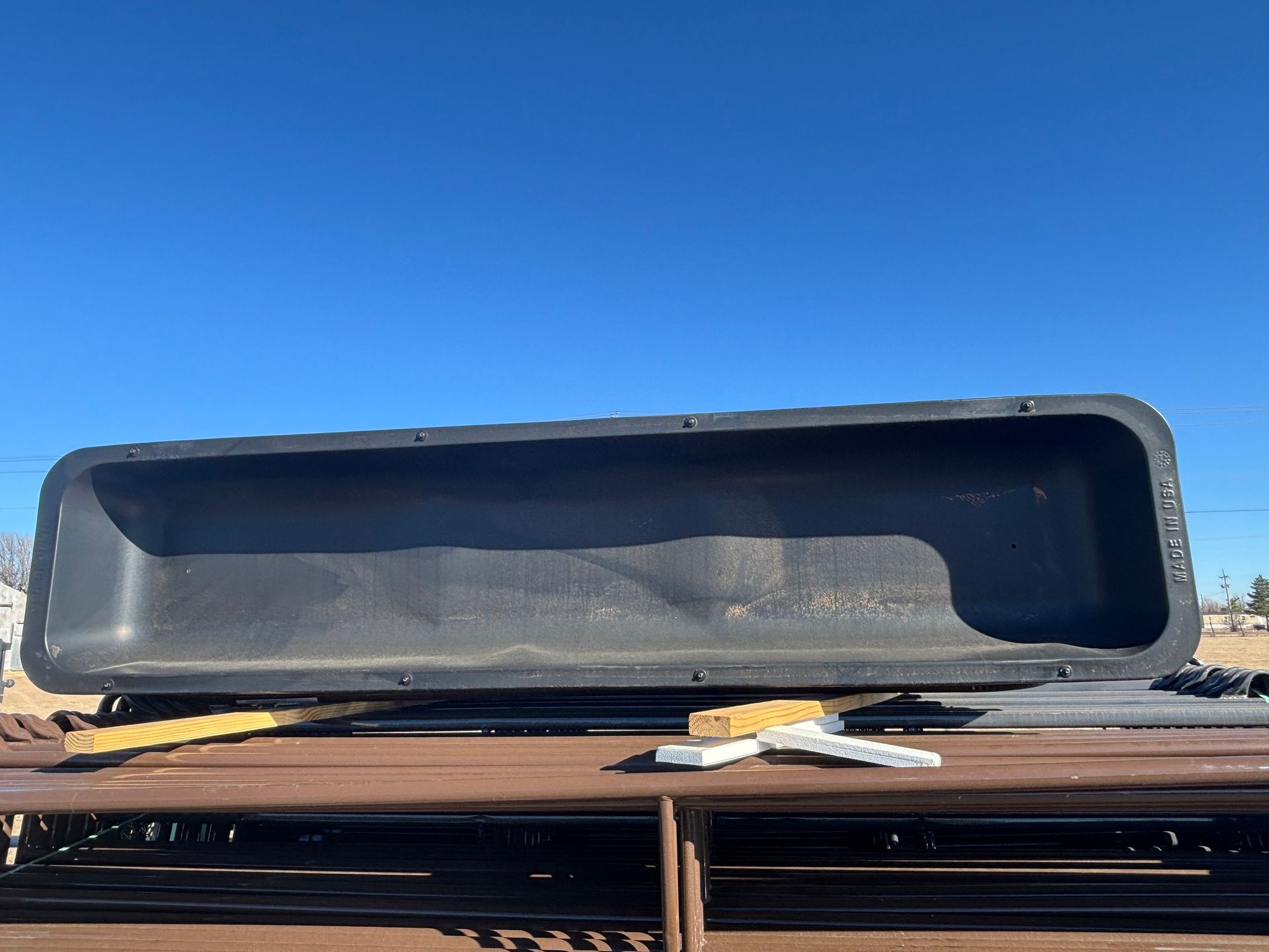 A long, rectangular, black plastic livestock trough sits atop a metal rack against a clear blue sky.