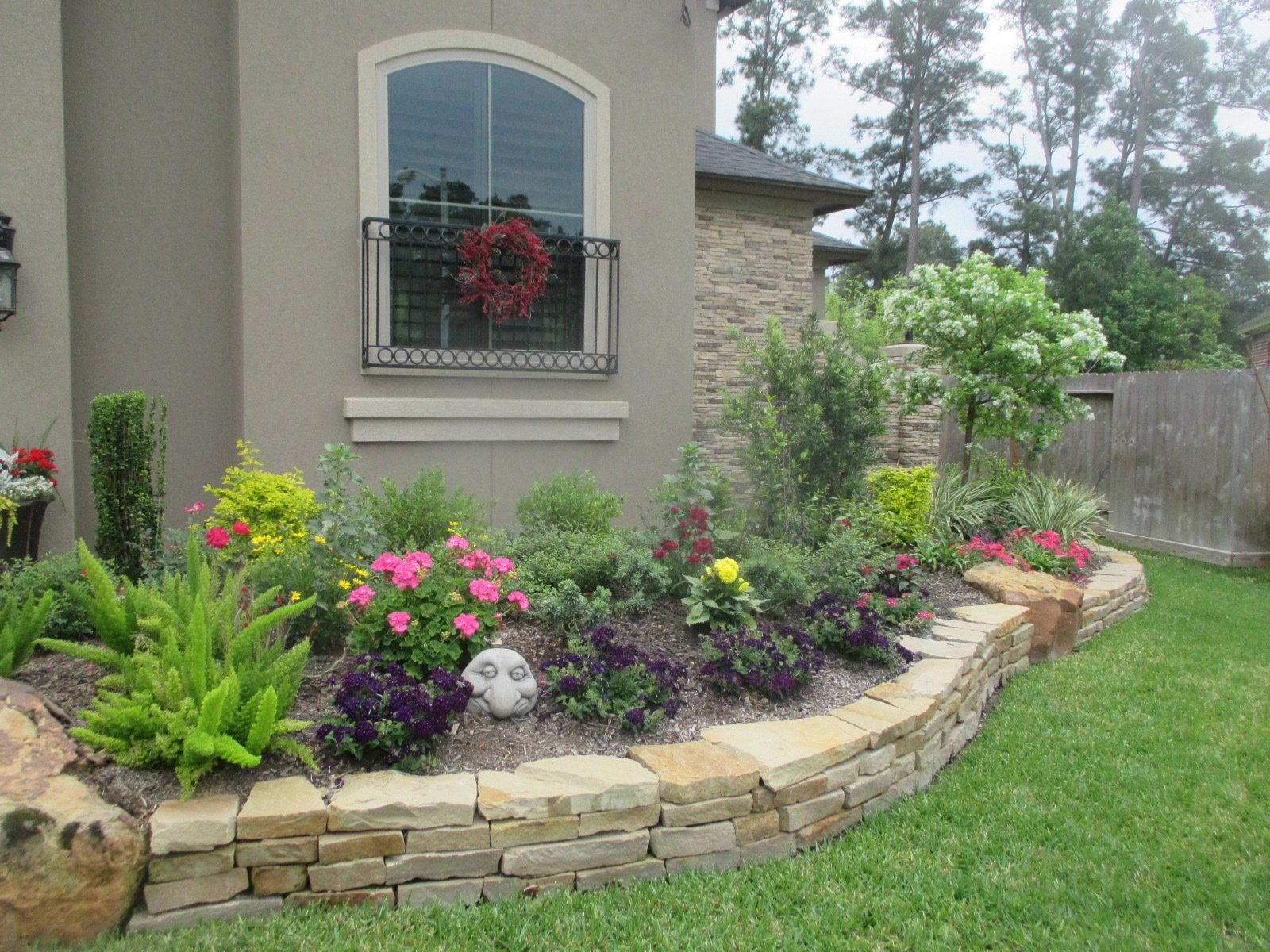 Curved garden bed with colorful flowers and stone edging beside a house window