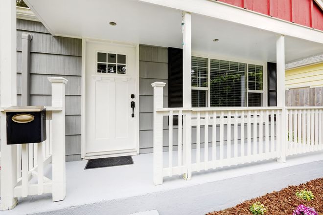 Front porch with white railing, white door, and gray siding under a red roof section