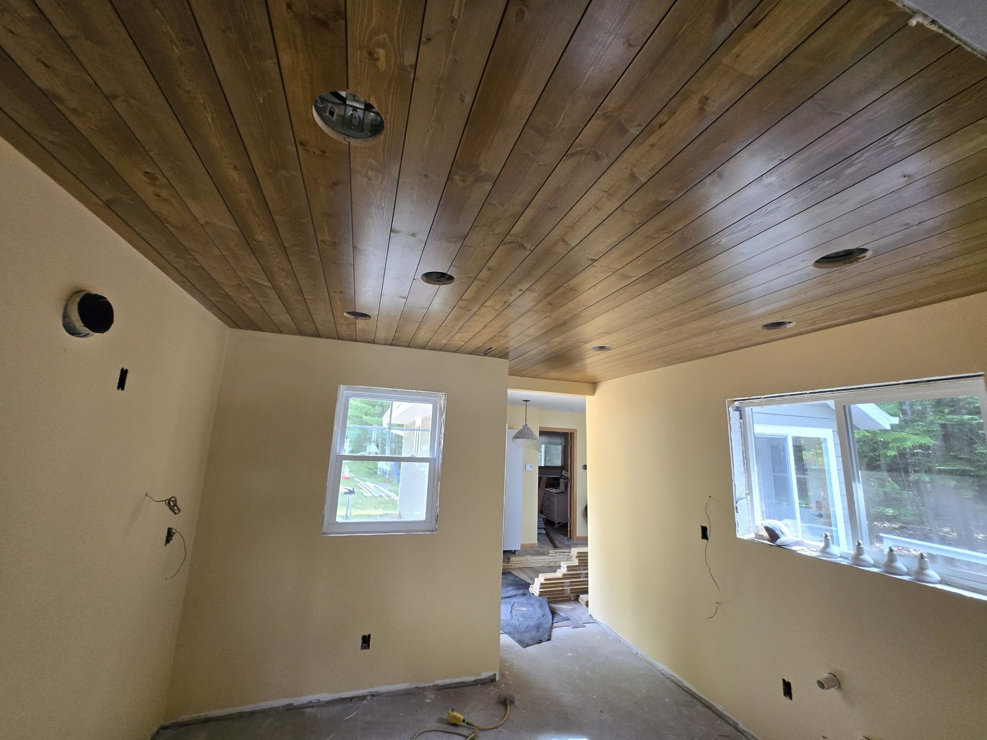 Empty room under renovation with wood ceiling, beige walls, and windows letting in daylight