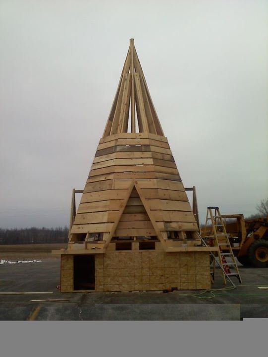Tall conical wooden structure under construction on a site with scaffolding and machinery