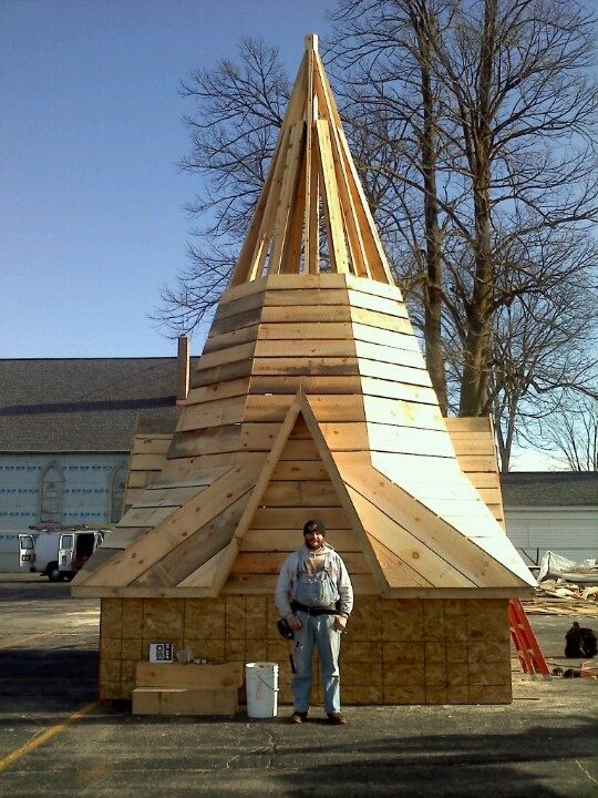 Wooden cone-shaped structure outdoors, with a person standing in front of it.