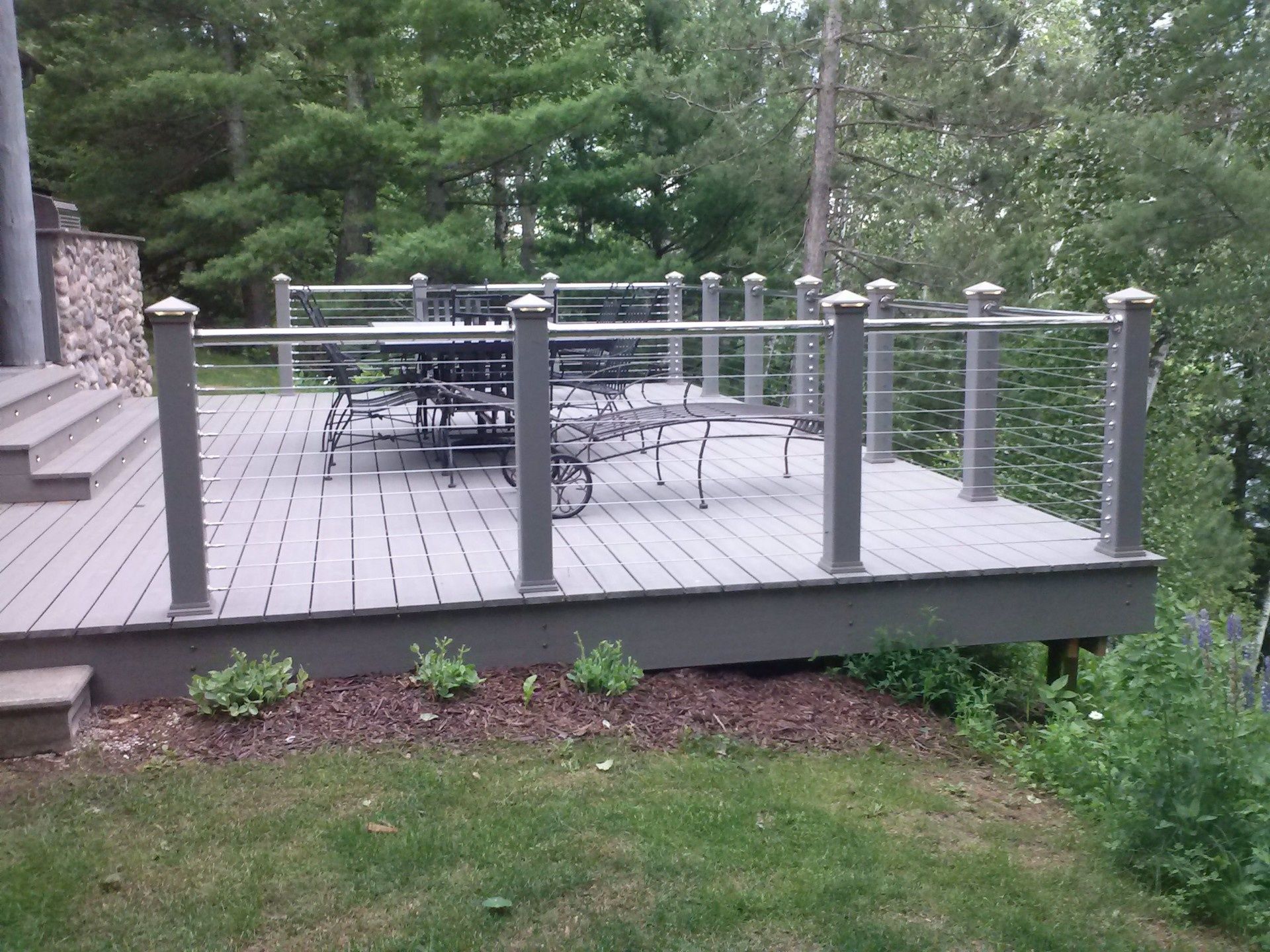 Wooden deck with metal cable railing and outdoor seating overlooking a wooded backyard