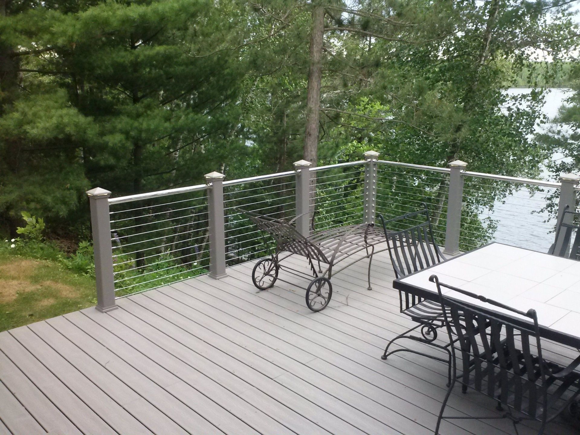 Deck with gray railing, black outdoor furniture, and a metal lounge chair overlooking trees and water.