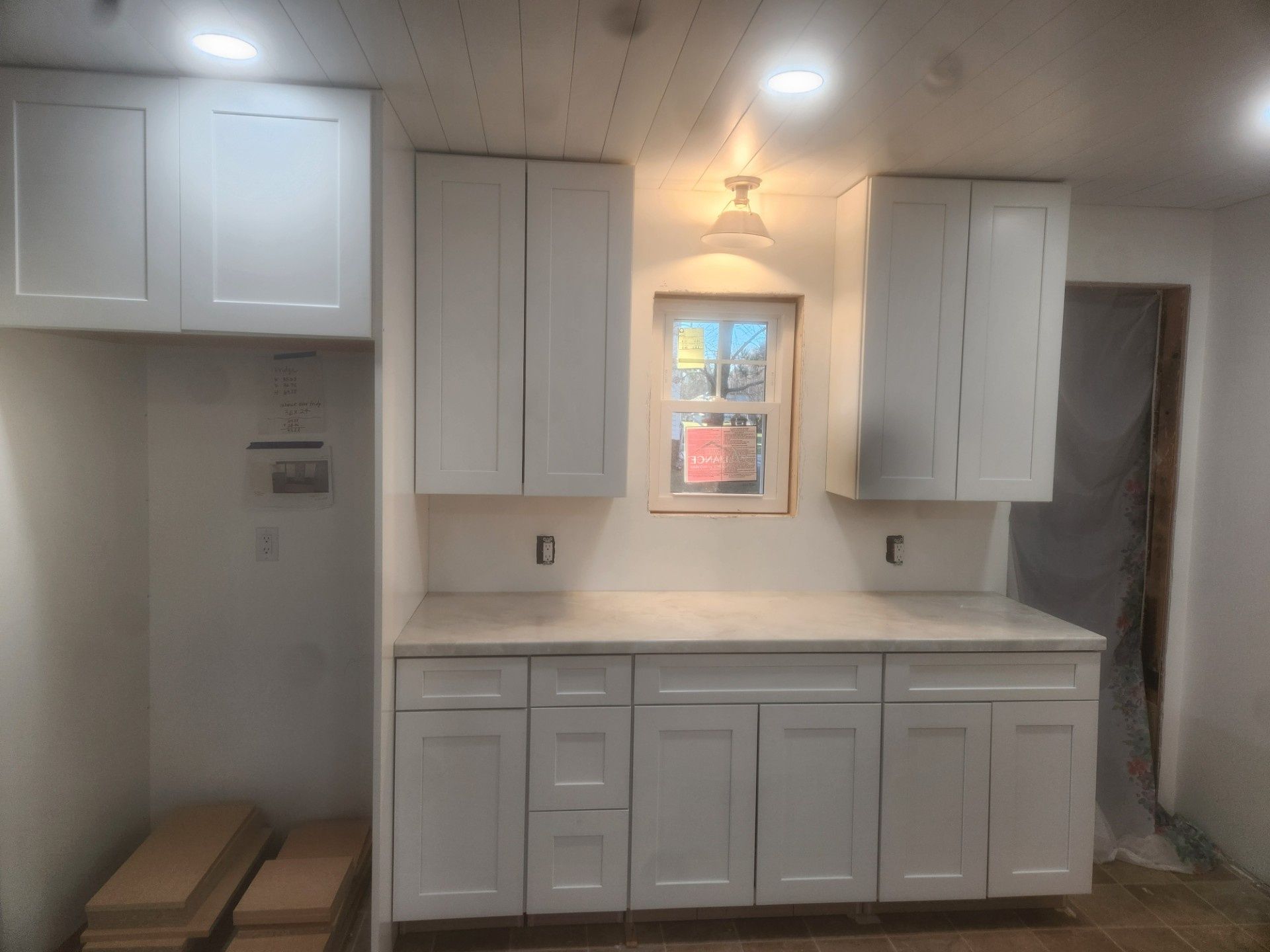 Small white kitchenette with cabinets, sink, countertop, and a window under a ceiling light.