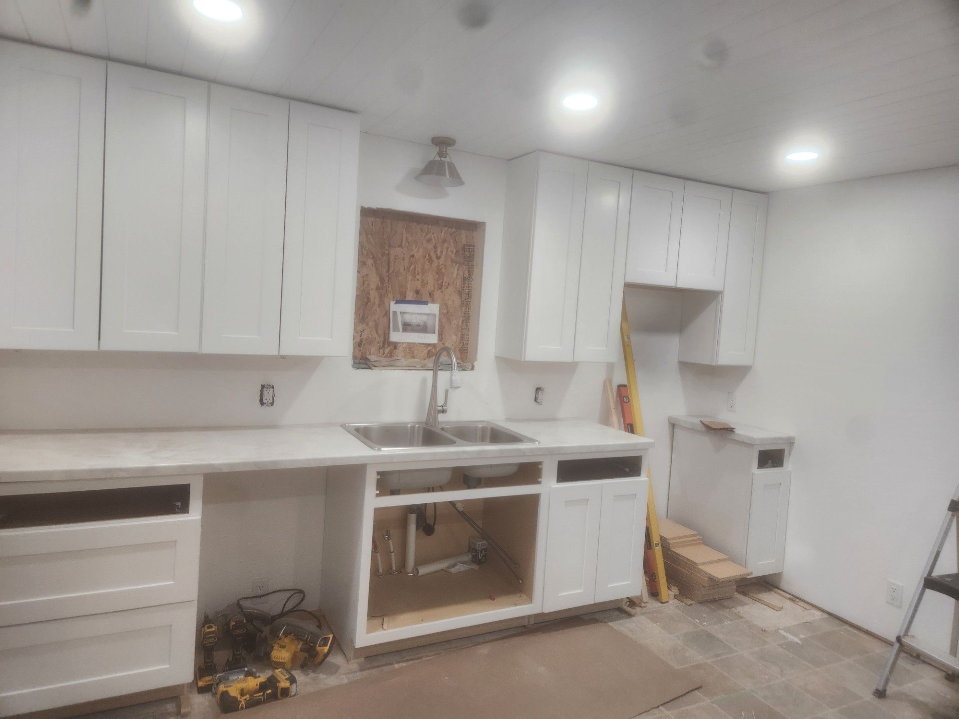 White kitchen under renovation with cabinets, sink, unfinished backsplash, and tools on the floor