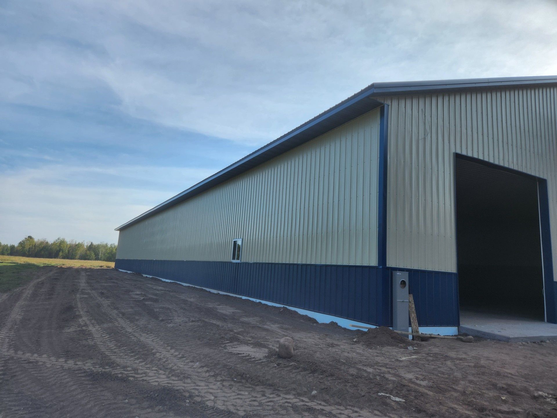 Long metal warehouse with open doorway on a gravel lot under a blue sky