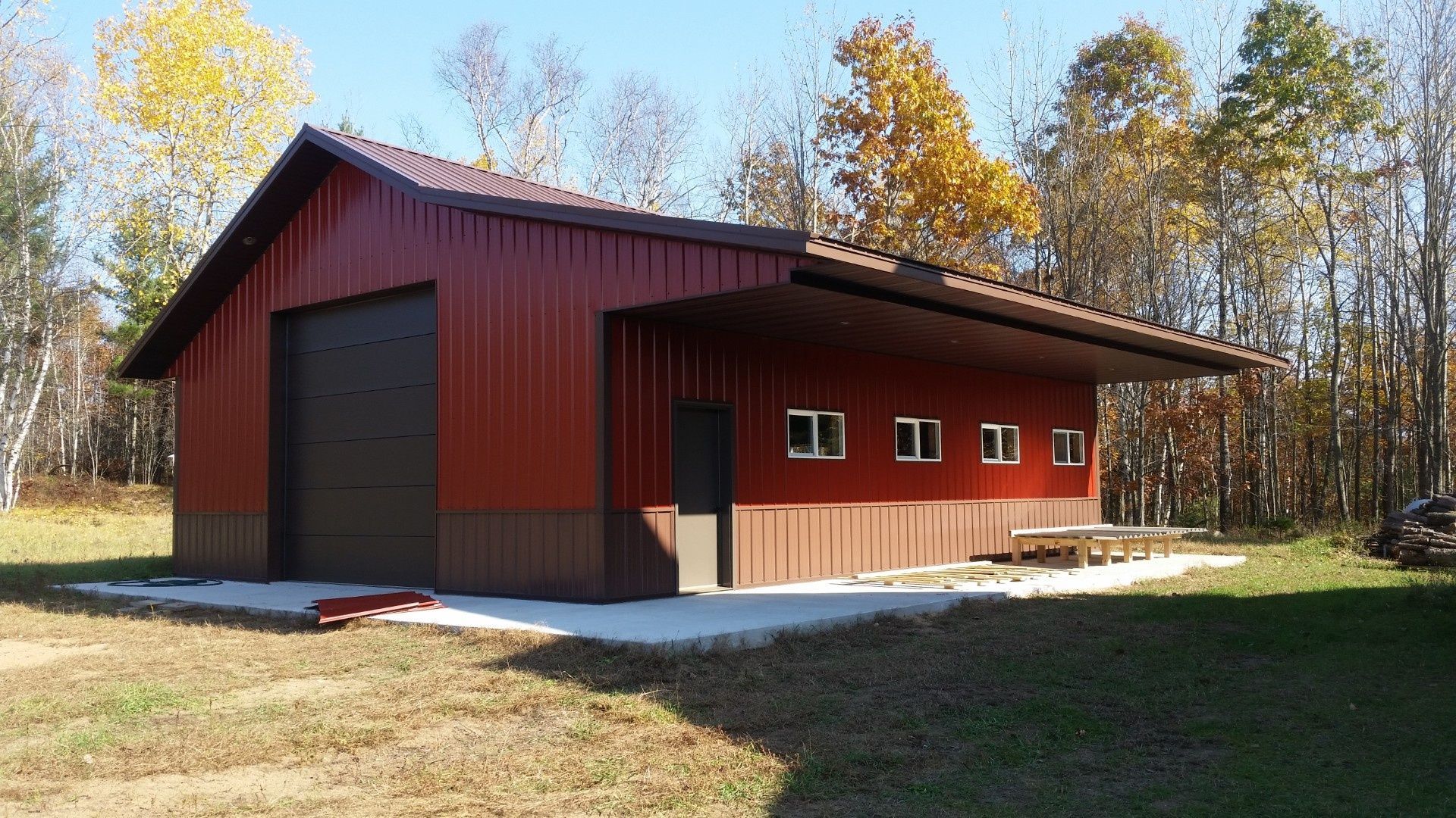 Red barn-style building with a large garage door in a sunny wooded clearing