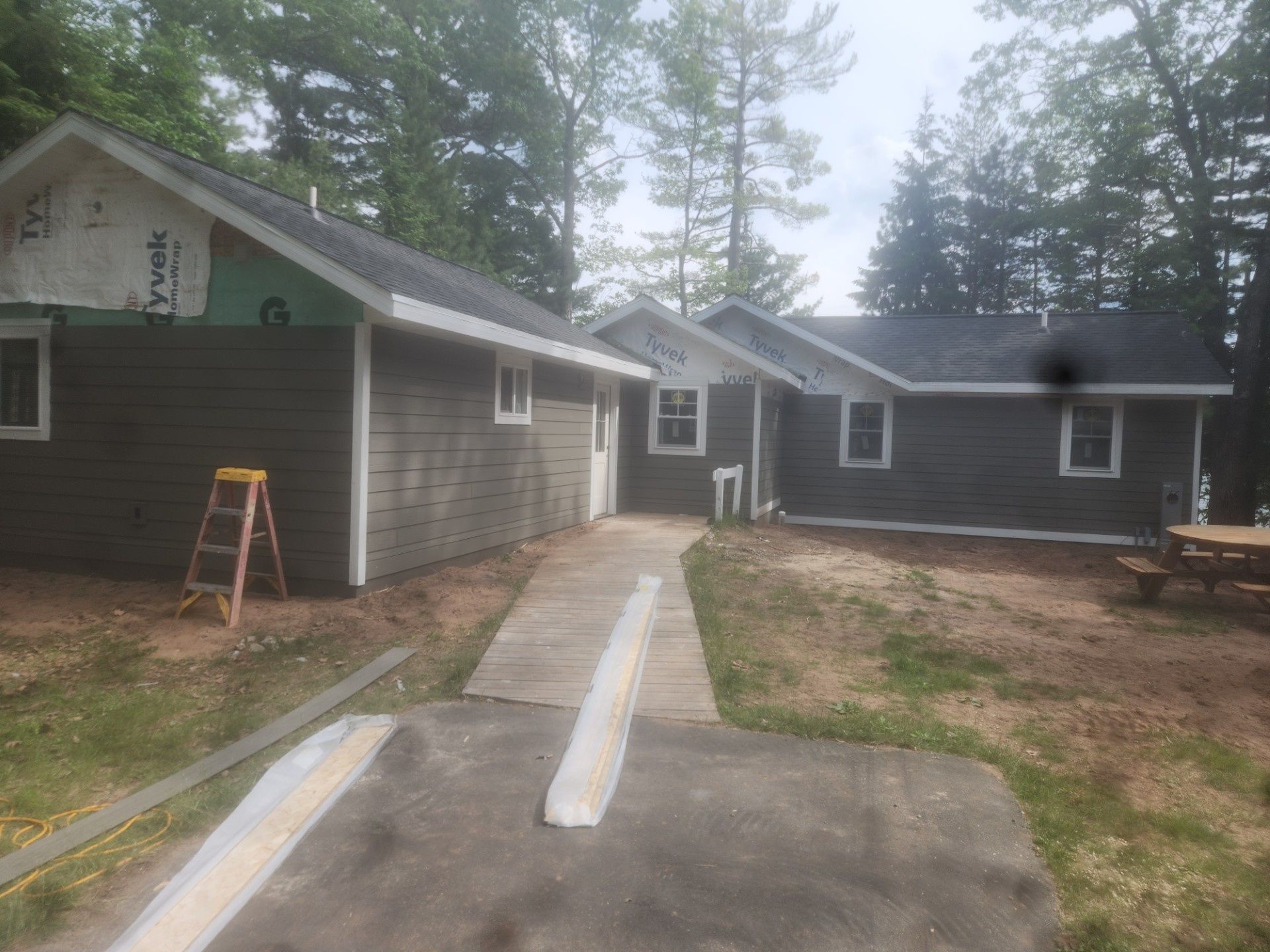House exterior with gray siding, a concrete walkway under construction, and a small ladder near the left wall