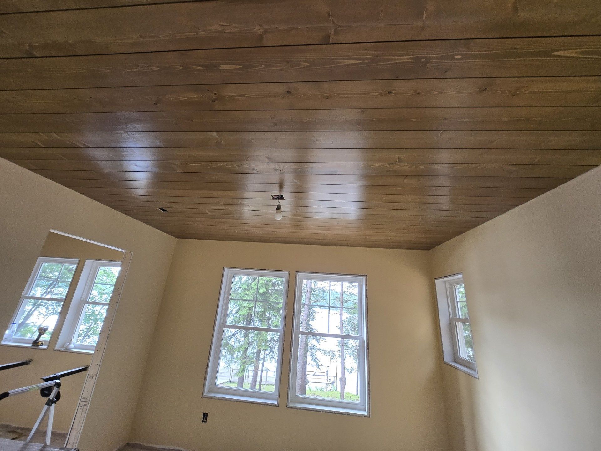 Empty room with beige walls, dark wood ceiling, and three sunlit windows.
