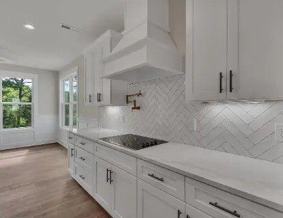 White kitchen with cabinets, countertops, and backsplash, with dark hardware and cooktop.