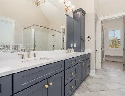 Bathroom with blue vanity, white countertop, glass shower, and a doorway to a closet.